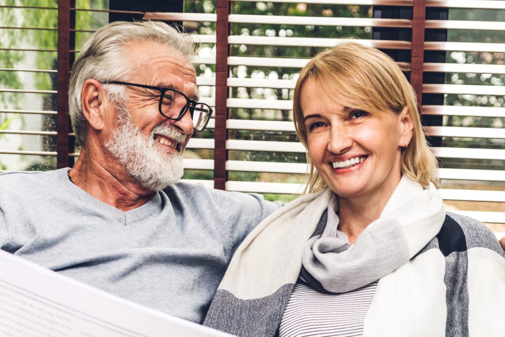Senior couple smiling while reviewing paperwork at home after deciding to sell a land contract for a lump sum of cash